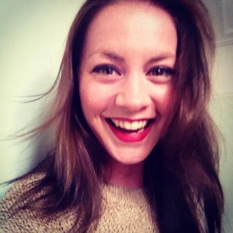 Portait of Molly Hodkinson laughing, facing the camera. She has shoulder length brown hair and is wearing a knitted top.