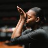 Benedicta Valentina dancing. She is facing left, with hands up to her face, palms open, with her eyes closed.