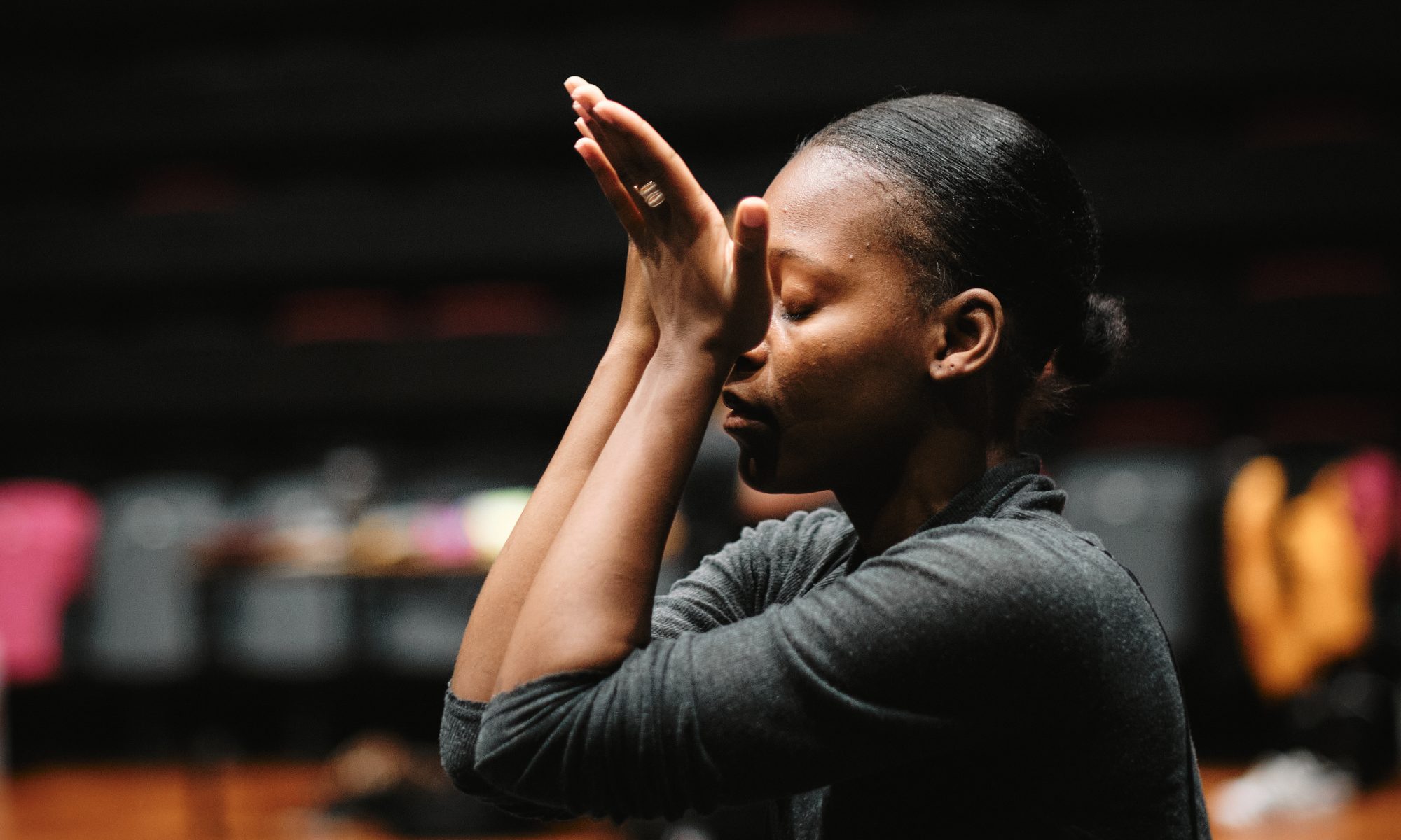 Benedicta Valentina dancing. She is facing left, with hands up to her face, palms open, with her eyes closed.