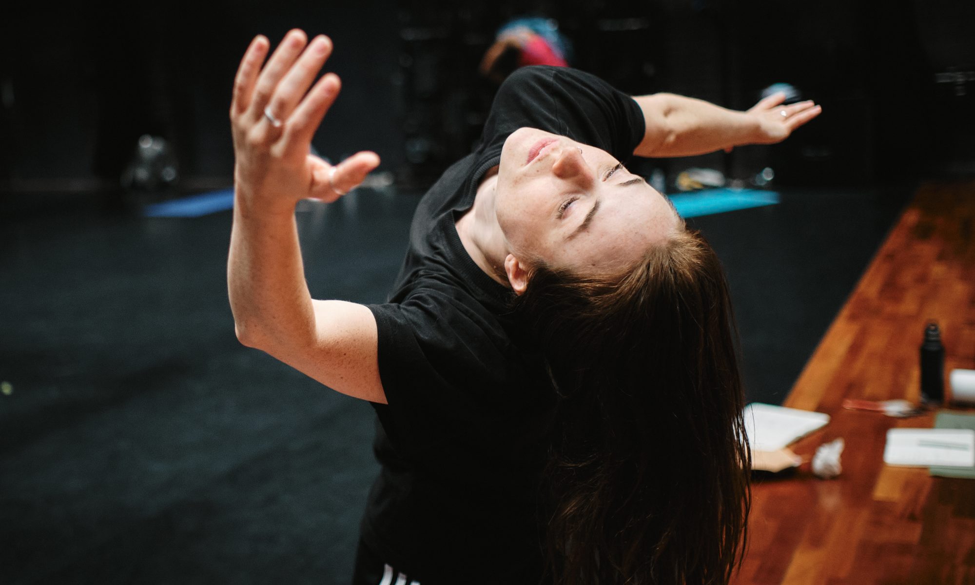 Alicia Meehan dancing. The picture is taken from a high angle, angled down at her face which is falling back. Her right arm twisting out to the side and her left arm stretching up towards the camera.