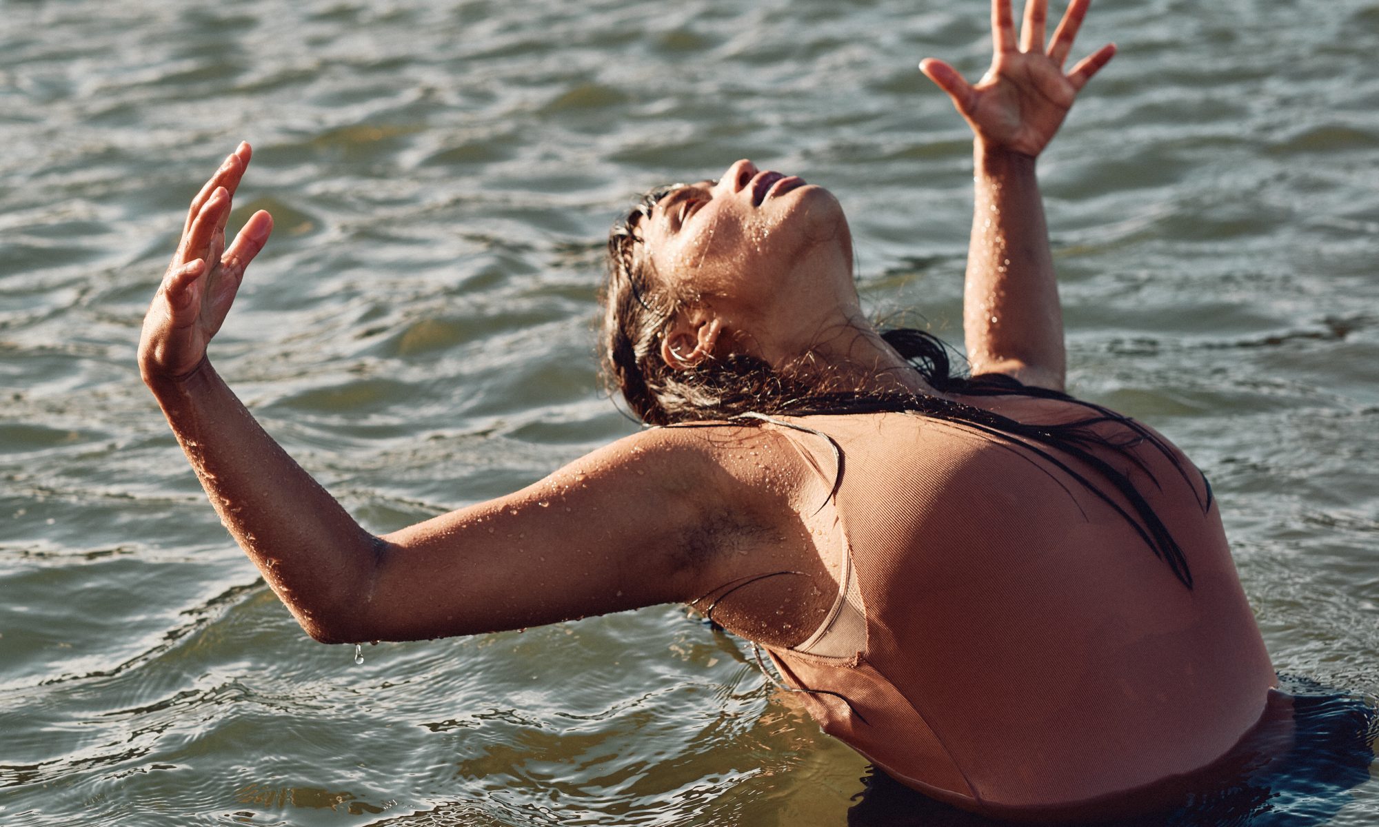 Jenna Anne Nathan dancing in the ocean for Grief Floats. She is waist deep in the ocean, leaning backwards, her arms wide in the air and her head falling back.