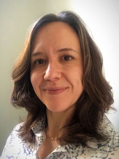 Headshot of Hillary Knight smiling. She has shoulder length brown hair and is wearing a blue and white button up shirt.