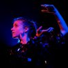 Jem Clancy dancing on stage. Her arm is up high behind her. She is lit by purple, pink and blue lighting.
