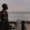 Patrick Ziza dressed in a mesh and sequin outfit standing by a railing looking at the ocean.