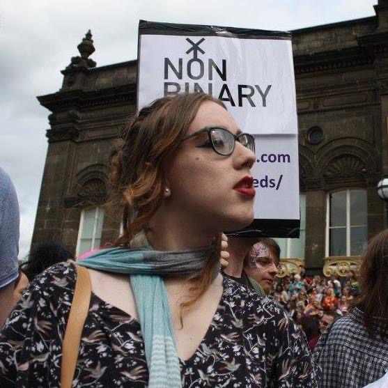 Esther O’Mara facing right during a pride festival. Behind her head is a Non Binary Leeds sign.
