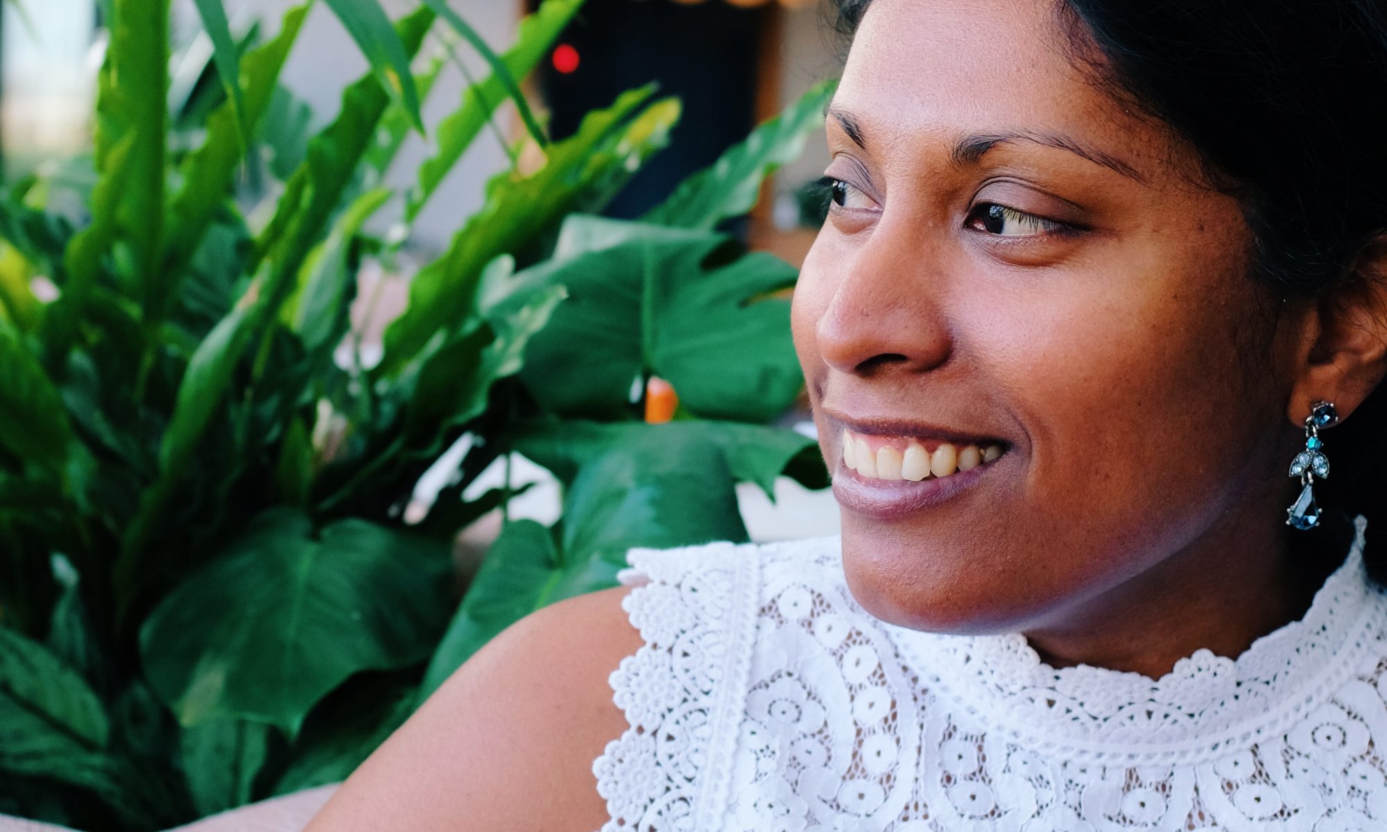 Sathya looking to the side smiling while sitting on a couch.