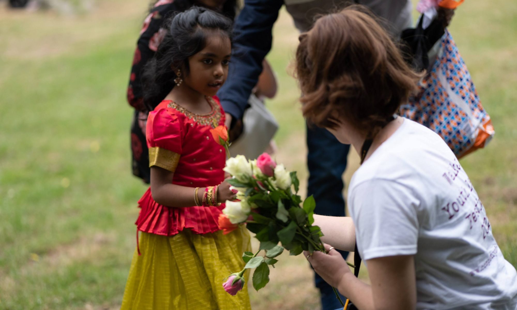 A person kneeling while giving flowers to a young child.