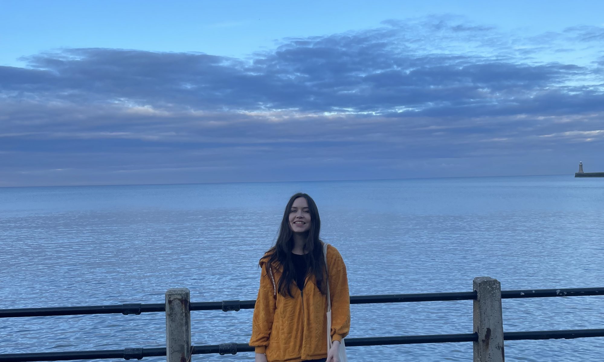 Katie smiling while standing in front of a railing with the ocean in the background.