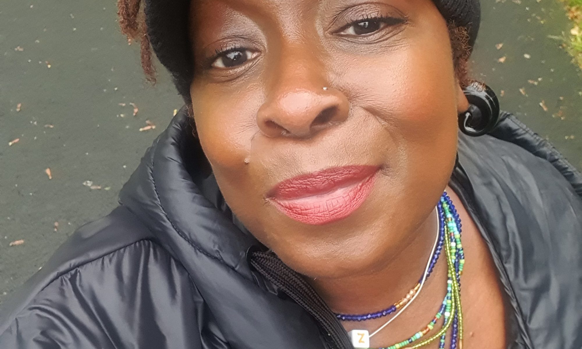 A headshot of Joanne. She is wearing smile on her face, colourful beads on her neck and a hat on her head.