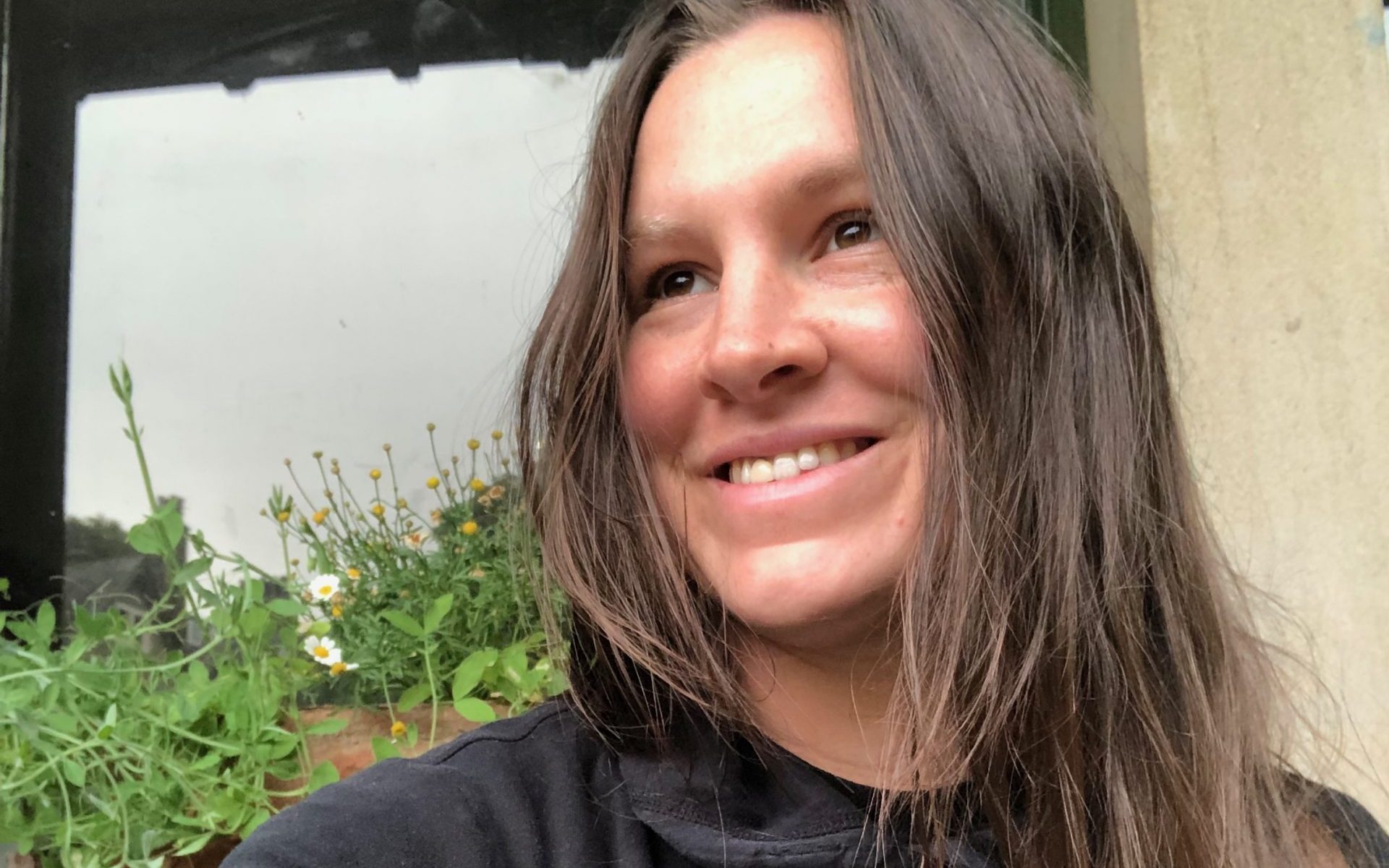 A headshot of Lily looking to the side smiling with plants in the background.