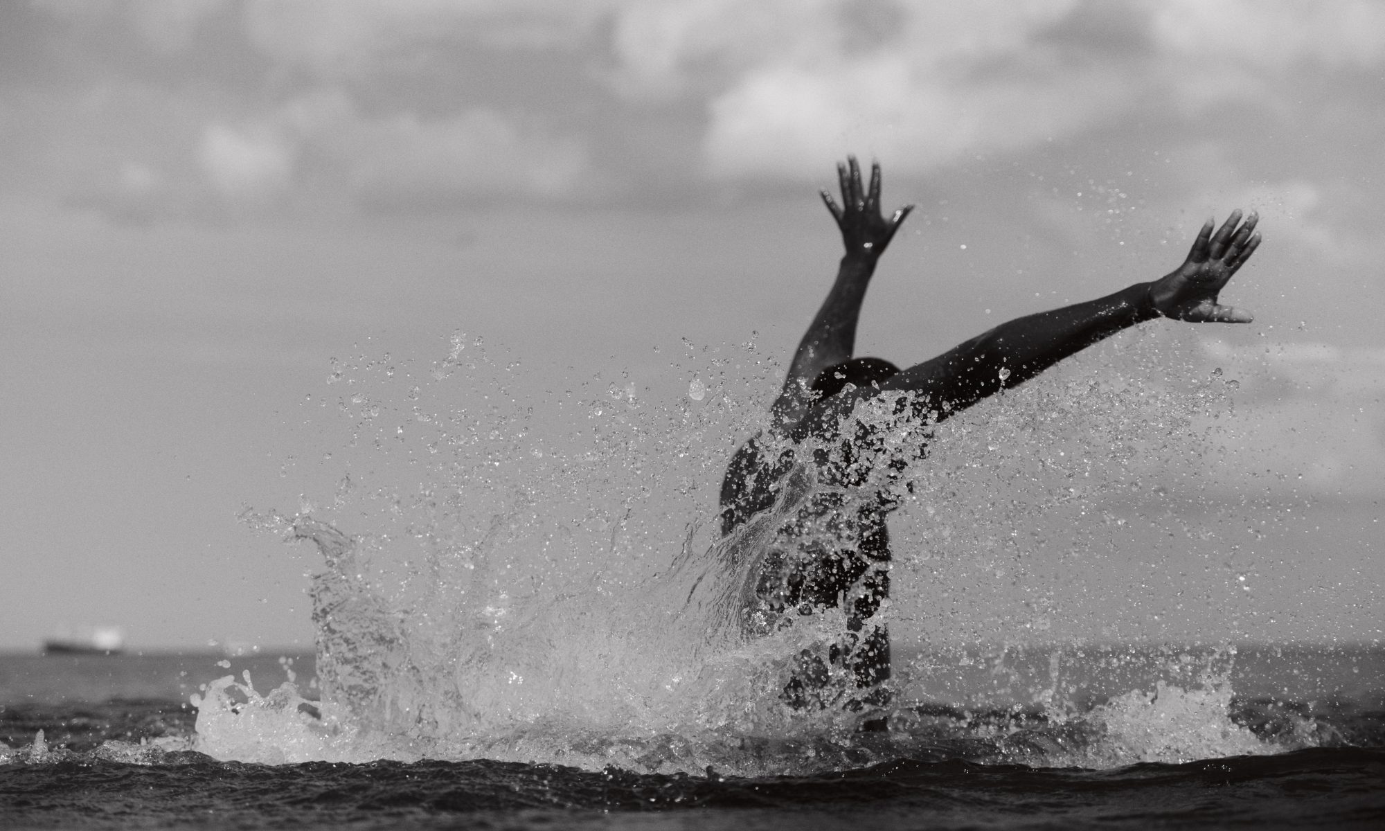 A dancer emerging from the ocean with their arms raised as water splashes around them