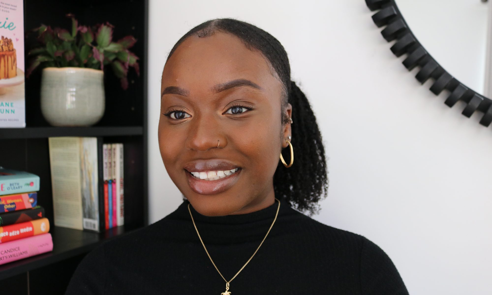 A portrait of Sekeenat smiling. She is wearing a black turtleneck top and a gold necklace.